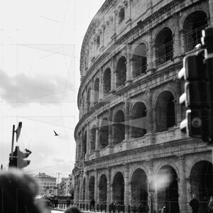 May include: A black and white photo of the Colosseum in Rome, Italy. The ancient Roman amphitheater is partially obscured by a traffic light and a group of people walking in front of it.