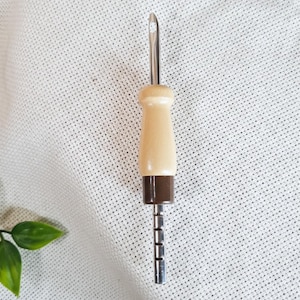 Può includere: Uno strumento per ago da punzone con un manico in legno marrone chiaro e una base marrone scuro. L'ago argentato ha un piccolo gancio. Questo strumento è progettato per l'uncinetto e il ricamo.