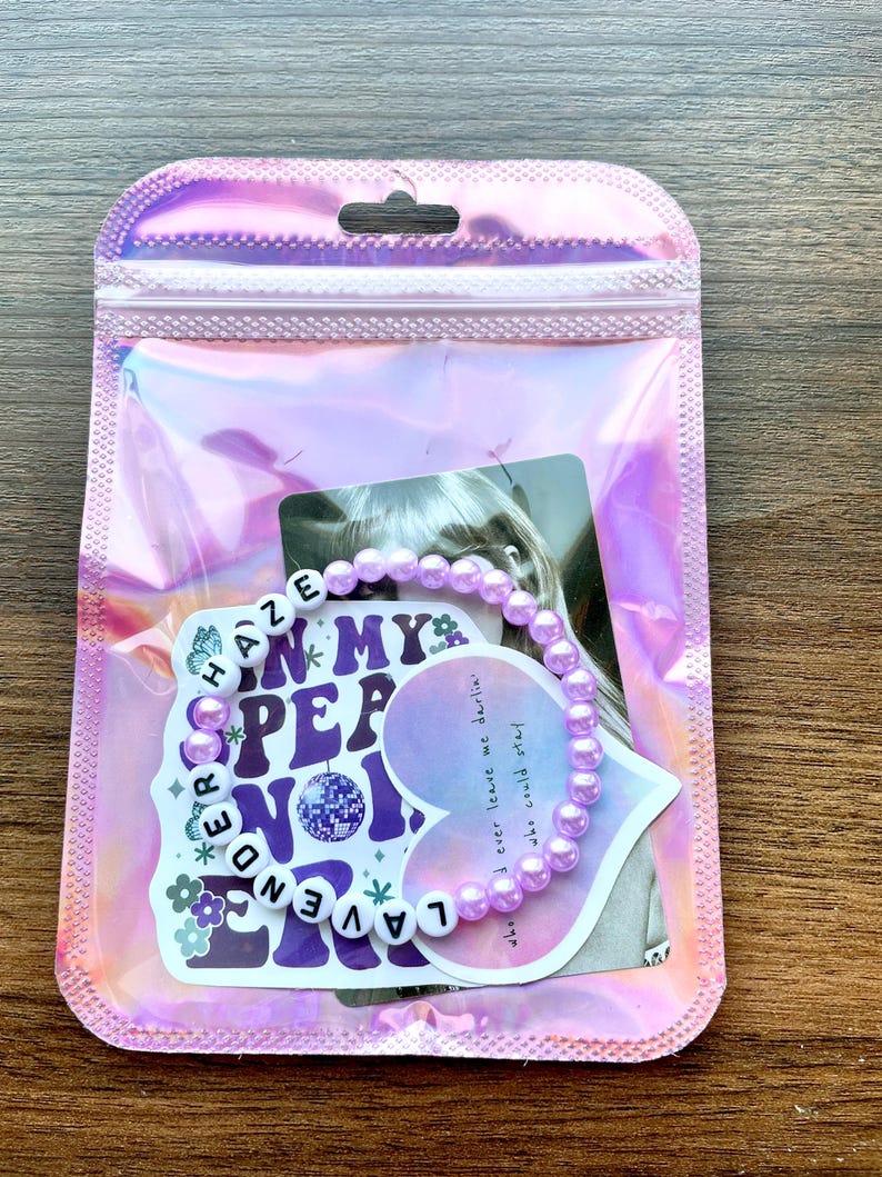 May include: A purple beaded bracelet with the words "Lavender Haze" and "In My  Pep No" on a white heart-shaped sticker. The sticker also includes the lyrics "who I ever leave me darlin' who could stay".