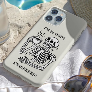 Puede incluir: Funda de tel&eacute;fono gris claro con un dise&ntilde;o de esqueleto en blanco y negro sosteniendo una taza de caf&eacute;. El texto "I'M BLOODY KNACKERED!" est&aacute; impreso en la funda. Gafas de sol y un sombrero de paja tambi&eacute;n son visibles.