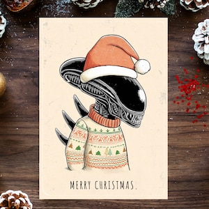 May include: A Christmas card featuring an alien wearing a Santa hat and a festive sweater. The alien is black with a detailed head and spiky back. The card reads "MERRY CHRISTMAS." The background includes pine cones, ornaments, and greenery.