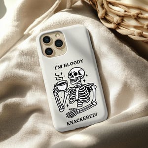 Puede incluir: Funda de tel&eacute;fono blanca con una ilustraci&oacute;n de esqueleto en blanco y negro bebiendo caf&eacute;. El texto "I'M BLOODY KNACKERED!" est&aacute; impreso en la funda. Dise&ntilde;ado para un smartphone con tres lentes.