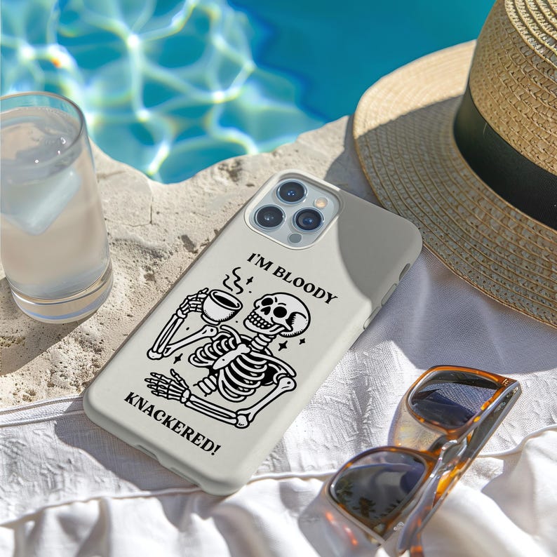 Puede incluir: Funda de tel&eacute;fono gris claro con un dise&ntilde;o de esqueleto en blanco y negro sosteniendo una taza de caf&eacute;. El texto "I'M BLOODY KNACKERED!" est&aacute; impreso en la funda. Gafas de sol y un sombrero de paja tambi&eacute;n son visibles.