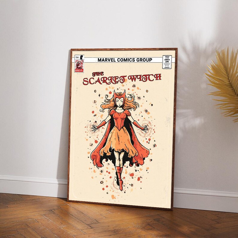 Op de afbeelding: Een ingelijste stripboekkunstprint met Scarlet Witch. De illustratie toont een vrouwelijk personage in een rood en oranje kostuum met een zwierige cape, tegen een cr&egrave;mekleurige achtergrond. De tekst "MARVEL COMICS GROUP" staat bovenaan.
