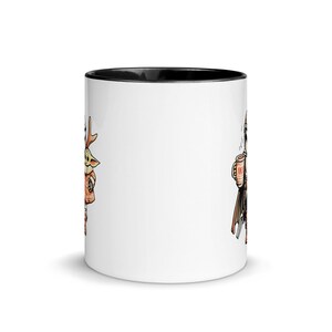 Op de afbeelding: Witte keramische mok met een zwarte binnenkant. De mok heeft cartoon illustraties aan elke kant. De ene kant toont een personage met geweien, de andere een figuur met een drankje. Een leuke, thematische koffiemok.