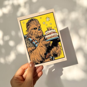 May include: A vintage-style birthday card featuring Chewbacca holding a cake with lit candles. The illustration has a yellow background with star accents. Chewbacca is depicted in brown and orange tones, wearing his signature bandolier.