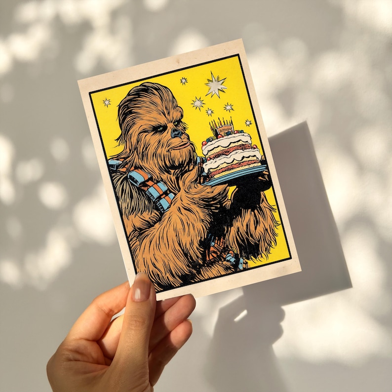 May include: A vintage-style birthday card featuring Chewbacca holding a cake with lit candles. The illustration has a yellow background with star accents. Chewbacca is depicted in brown and orange tones, wearing his signature bandolier.
