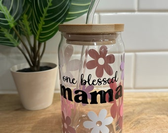 May include: A clear glass reusable water bottle with a bamboo lid and a straw. The bottle has a floral design with pink, white, and purple flowers. The text "one blessed mama" is printed on the bottle in black.