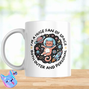 以下が含まれることがあります： 惑星と星に囲まれた宇宙服を着た猫の白黒イラストが描かれた白いセラミックマグカップ。マグカップのテキストは「I'm a huge fan of space both outer and personal.」です。