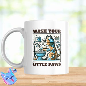 Op de afbeelding: Witte keramische mok met een kleurrijke illustratie van een kat die zijn poten wast in een wastafel. De tekst "WASH YOUR LITTLE PAWS" staat op de mok gedrukt.