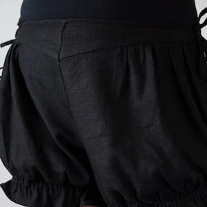 May include: Black cotton shorts with a ruffled hem and a gathered, puffed design. The shorts have a high waist and a fitted waistband.