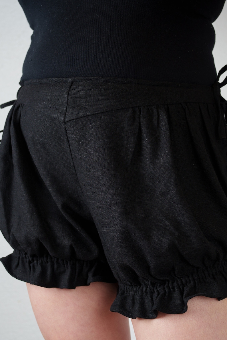 May include: Black cotton shorts with a ruffled hem and a gathered, puffed design. The shorts have a high waist and a fitted waistband.
