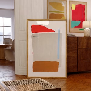 May include: Three framed abstract art prints with geometric shapes in red, orange, yellow, blue, and gray. The prints are hanging on a white wall above a wooden dresser.