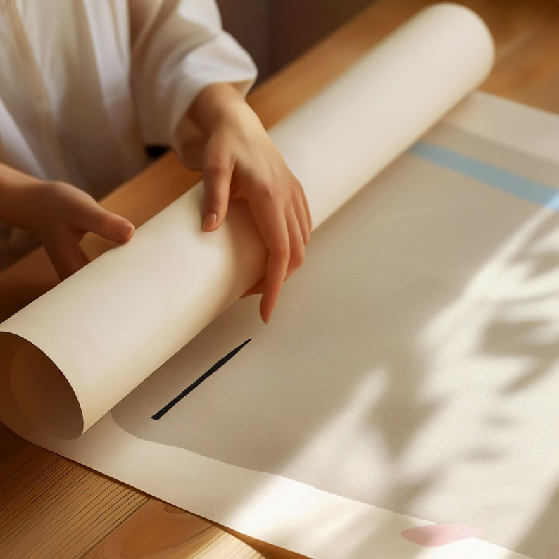May include: A white rolled up poster or paper being unrolled by a hand. The poster is on a light brown wooden surface.