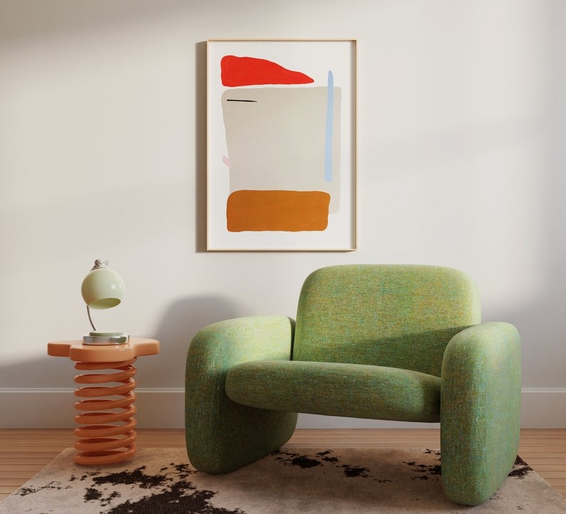 May include: A green armchair with a textured fabric. The armchair is in front of a white wall with a framed abstract painting with orange, red, and blue shapes. A small orange side table with a spring design is next to the armchair. A white lamp with a white shade is on the side table.