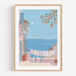 Puede incluir: Una impresión artística enmarcada representa una escena costera con un balcón, ropa tendida y vista al mar. La obra presenta un edificio rosa, cielo azul y un tendedero con prendas colgadas. Una rama de limonero cuelga de la esquina superior derecha. El tema general es una estética mediterránea soleada.