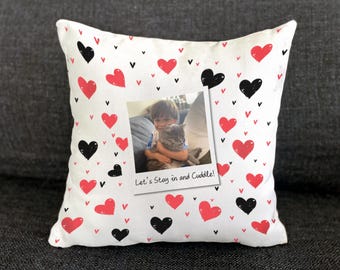 May include: White throw pillow with a pattern of red and black hearts and small black arrow shapes. A photo of a child holding a cat is in the center, with the text "Let's Stay in and Cuddle!"