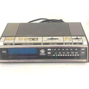 Puede incluir: Una radio reloj digital AM/FM General Electric vintage. El reloj tiene una pantalla LED azul que muestra 88:88. Cuenta con botones para repetición, suspensión y configuración de pantalla, junto con controles de radio para volumen y selección de banda. La radio tiene un diseño negro y plateado.