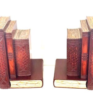 May include: A pair of bookends, each designed to resemble a stack of three upright books resting on a single horizontal book base. The bookends feature a dark reddish-brown finish with intricate cross-hatched patterns and cream-colored page edges.