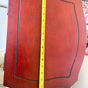 May include: A reddish-brown wooden cabinet door with a black trim and a yellow measuring tape. The door is approximately 46 cm tall. The door has a rectangular panel with a curved top and bottom.