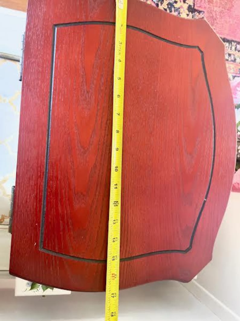 May include: A reddish-brown wooden cabinet door with a black trim and a yellow measuring tape. The door is approximately 46 cm tall. The door has a rectangular panel with a curved top and bottom.