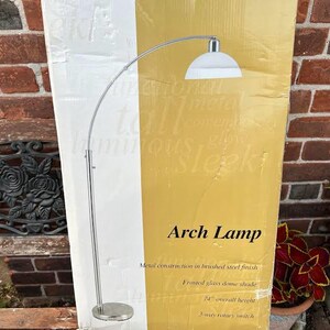 May include: An arch lamp with a brushed steel finish and a frosted glass dome shade. The packaging box displays the text Arch Lamp, metal construction in brushed steel finish, frosted glass dome shade, 74" overall height, and 3-way rotary switch.