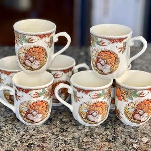 以下が含まれることがあります： 秋の紅葉と果物に囲まれた七面鳥のカラフルなグラフィックが繰り返される、6個の白いセラミック製マグカップのセット。各マグカップには湾曲したハンドルがあり、縁の周りには装飾的なボーダーパターンが施されています。
