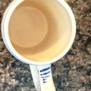 May include: White ceramic mug with a beige interior and a white handle. The handle is decorated with blue vertical lines and dots. The rim of the mug has a thin blue line.