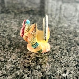 May include: A ceramic turkey figurine with a colorful design. The turkey has a red wattle, a blue head, and a yellow and orange body. The figurine is likely a decorative item for Thanksgiving.