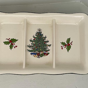 Könnte beinhalten: Cremefarbene rechteckige Servierschale mit drei Fächern und schwarzem Rand. In der Mitte befindet sich ein Weihnachtsbaum-Design, flankiert von Stechpalmenzweigen mit roten Beeren. Ein festliches Servierstück.
