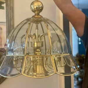 May include: A vintage brass and glass chandelier with a domed, petal-shaped glass shade. The fixture has a gold finish and features multiple light bulbs. The chandelier is suspended from a ceiling fixture.
