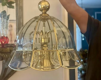 May include: A vintage brass and glass chandelier with a domed, petal-shaped glass shade. The fixture has a gold finish and features multiple light bulbs. The chandelier is suspended from a ceiling fixture.