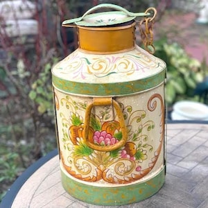 Könnte beinhalten: Eine zylindrische Milchkanne aus Metall mit cremefarbener Basis, verziert mit handgemalten Blumenmotiven in Orange, Pink und Grün. Sie verfügt über einen senfgelben Hals, einen Klappdeckel mit kleinem Griff und einen stabilen gelben Seitengriff.