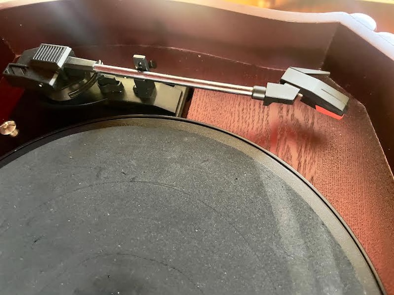 May include: Close-up of a vintage record player. The turntable features a black platter and a silver tone arm with a black headshell. The wooden cabinet has a dark brown finish.