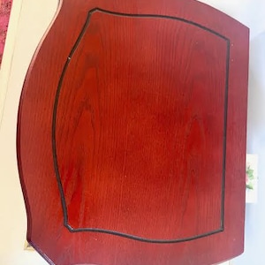 May include: A reddish-brown wooden table with a black trim. The table has a unique shape with curved edges and a rectangular inset. The wood grain is visible, and the table appears to be well-maintained.