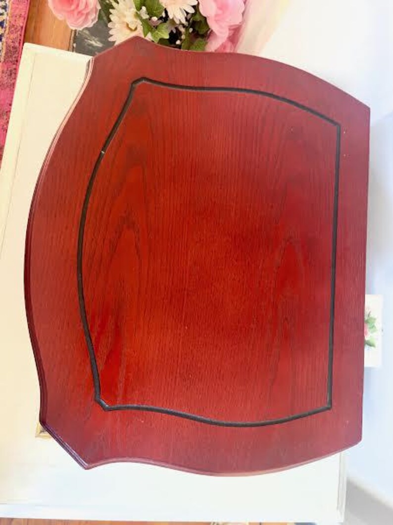 May include: A reddish-brown wooden table with a black trim. The table has a unique shape with curved edges and a rectangular inset. The wood grain is visible, and the table appears to be well-maintained.