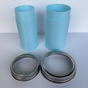May include: Two light blue cylindrical containers with a slightly wider top, paired with two silver metal jar rings. The containers are smooth and stand upright. The rings have a threaded design.