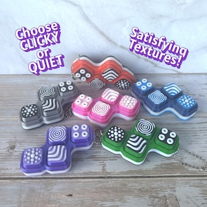 May include: A collection of colorful fidget toys in various shapes and designs. The toys feature a variety of textures and patterns, with options for clicky or quiet operation. The color palette includes red, gray, pink, blue, green, and purple.