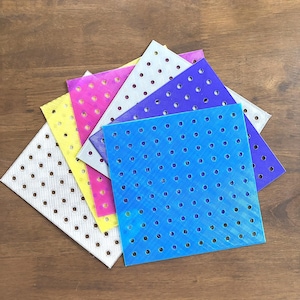 May include: A collection of colorful, square plastic sheets with evenly spaced holes. The sheets are in various colors, including blue, purple, pink, yellow, and white. The sheets are arranged in a fan shape, with the holes visible.