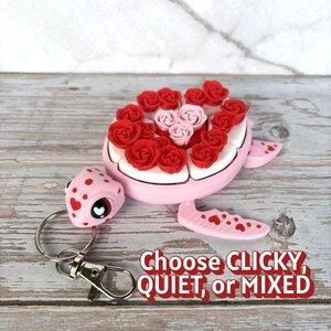 May include: A pink turtle-shaped keychain with red and pink rose accents. The turtle's shell is adorned with red roses, while the center features pink roses. The turtle's head and flippers have heart details. The text "Choose CLICKY, QUIET, or MIXED" is visible.