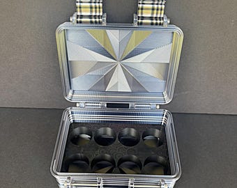 May include: An open, clear acrylic case with a geometric starburst design on the lid. The case has a black interior with circular cutouts. The hinges and clasps have a plaid pattern.