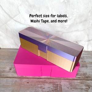 May include: A two-piece storage box set. The top box is rectangular with a gold base, purple accents, and a patterned lid. The bottom box is a bright pink, rectangular container. Text on the image reads: Perfect size for labels, Washi Tape, and more!