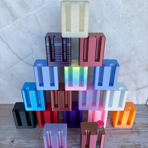 May include: A collection of rectangular, multi-colored plastic stands arranged in a pyramid shape. Each stand features two vertical slots designed for holding small items. The colors include black, blue, red, purple, pink, orange, white, and gradient.
