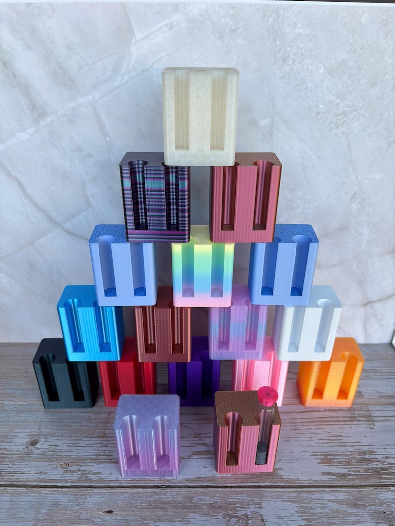 May include: A collection of rectangular, multi-colored plastic stands arranged in a pyramid shape. Each stand features two vertical slots designed for holding small items. The colors include black, blue, red, purple, pink, orange, white, and gradient.