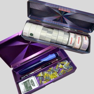 May include: Open purple and blue medical supply case with various items. The top section holds rolls of white tape and labels with the text "NIIMBOT". The bottom section contains pens, needles, and alcohol prep pads.