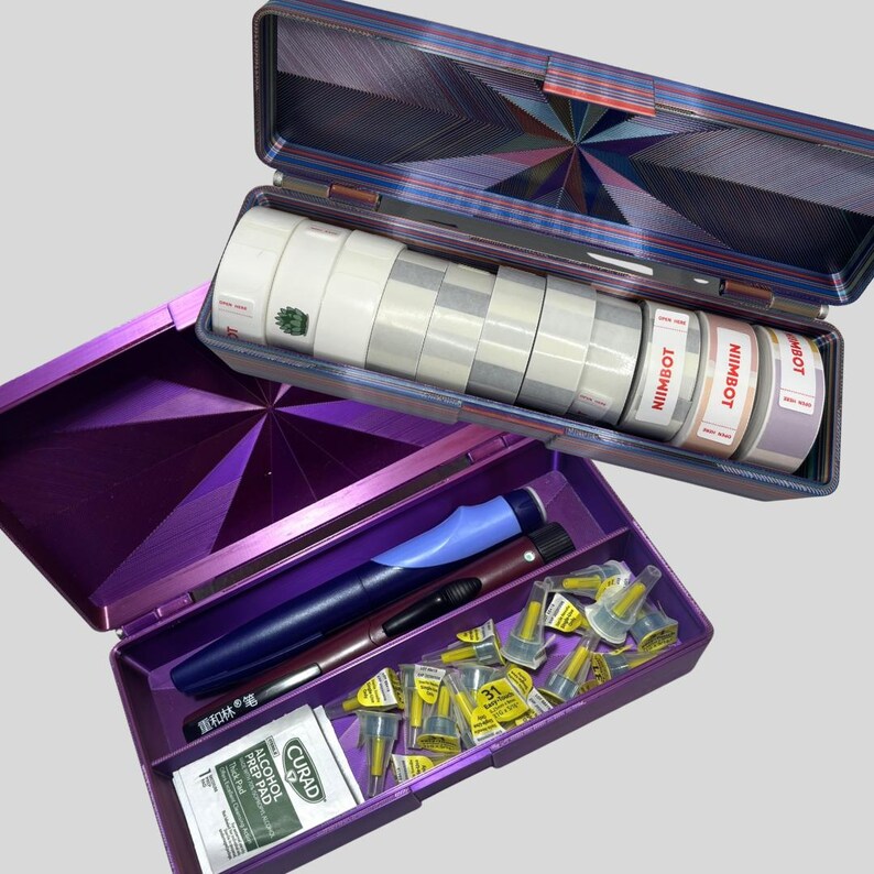 May include: Open purple and blue medical supply case with various items. The top section holds rolls of white tape and labels with the text "NIIMBOT". The bottom section contains pens, needles, and alcohol prep pads.