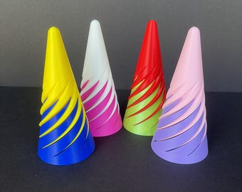 May include: Four colorful, cone-shaped objects with spiral designs. The cones are yellow and blue, white and pink, red and green, and pink and purple. The objects are arranged on a dark surface.
