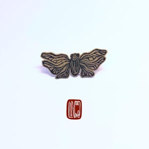 May include: A black and white line drawing of a butterfly with intricate details. The butterfly is printed on a light brown background. The image includes a red stamp with the word "LINA" in black.