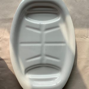May include: White oval serving platter with blue floral accents. The platter has a raised center section with grooves and a decorative floral pattern at each end. A classic piece for serving food.