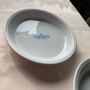 May include: A white pie plate with a blue floral design. The design features three stylized flowers with five petals each.